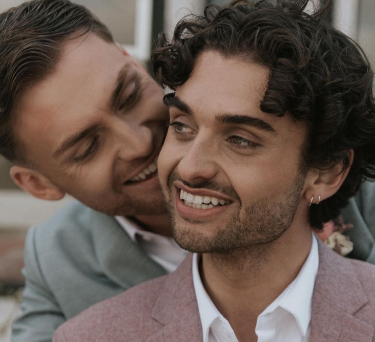 Grooms embrace outdoors whilst smiling lovingly