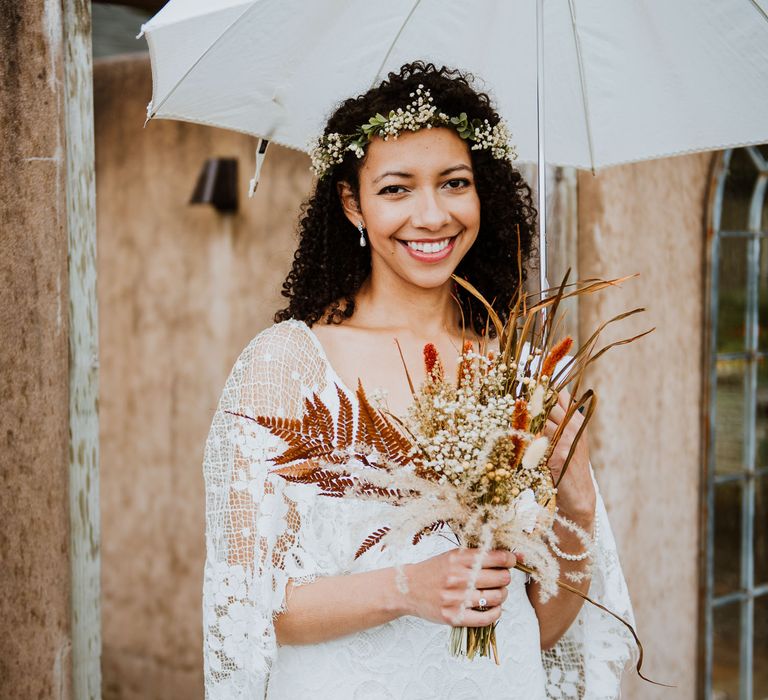 Bride carries dried floral bouquet and umbrella wearing floral crown and Grace Loves Lace wedding gown