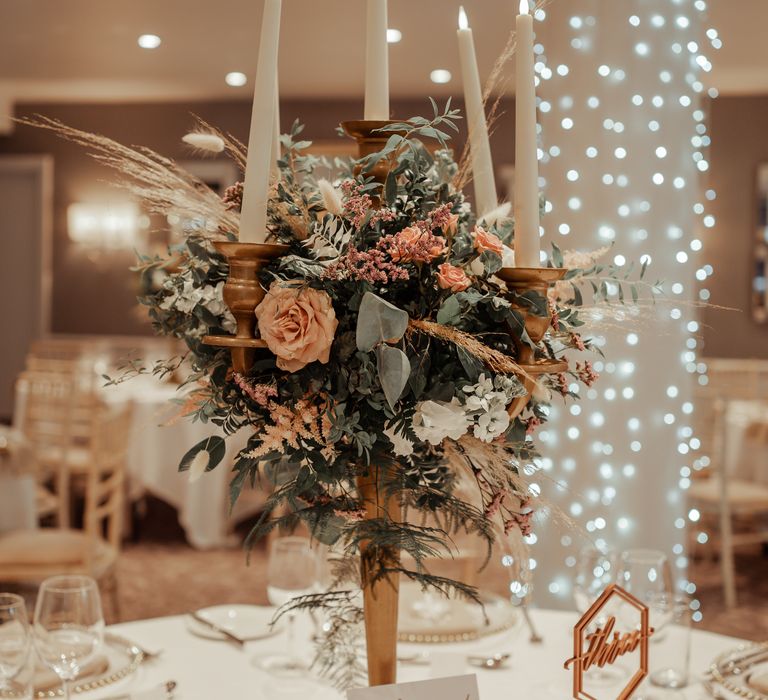 Elegant and classic decor with candlestick holder surrounded by roses and green foliage 