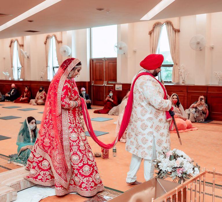 Bride & groom during traditional Sikh ceremony as bride holds grooms sash and walks around the room as the Lavan is read