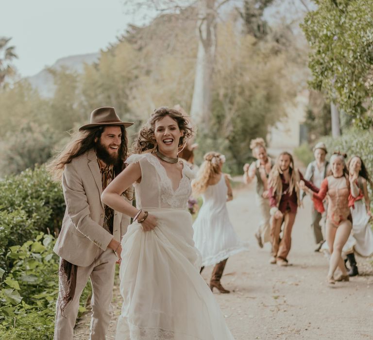 Bride & groom walk together as the beautiful countryside can be seen behind them and circus performers dance alongside them