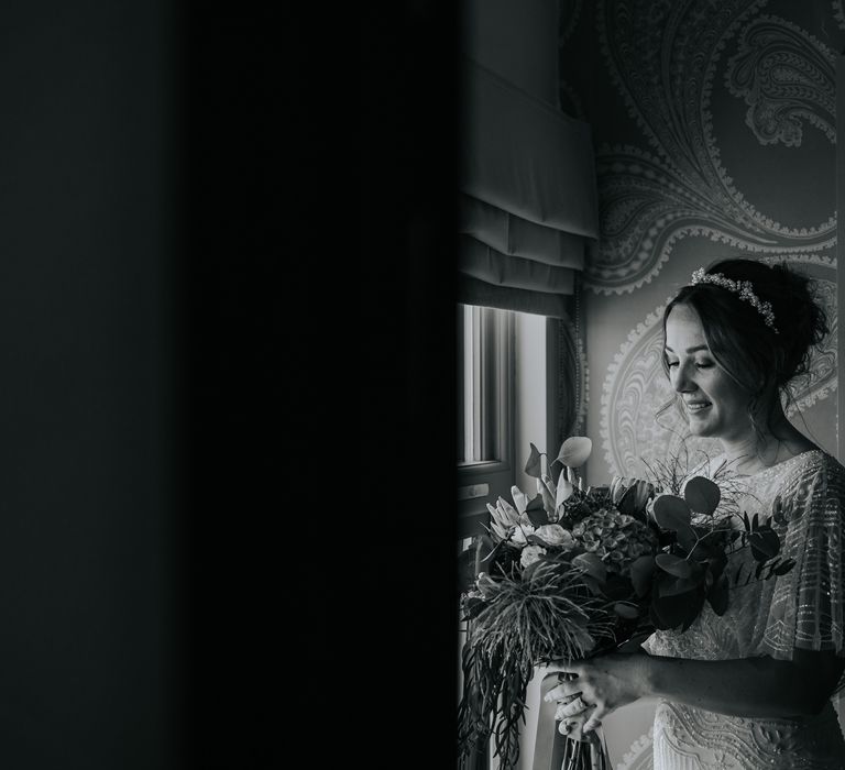 Bride looks down at her floral bouquet in black & white image before wedding ceremony