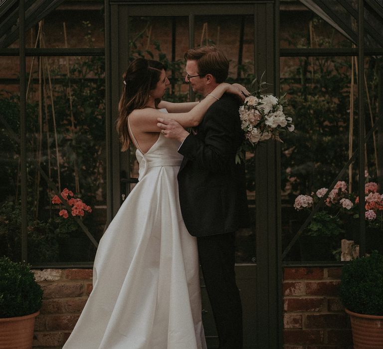 Bride & groom embrace outside greenhouse at Elmore Court on their wedding day