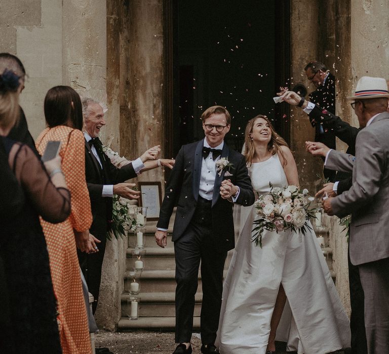 Bride & groom leave wedding ceremony as confetti is thrown around them