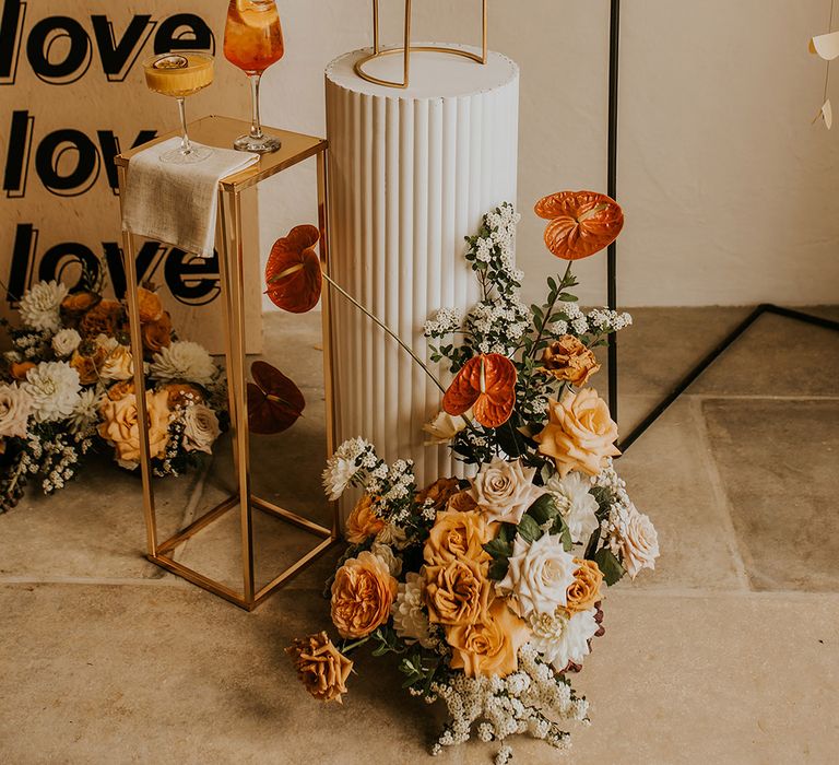 Monumental wedding cake on a plinth surrounded by orange and yellow flowers, a love sign and cocktails 