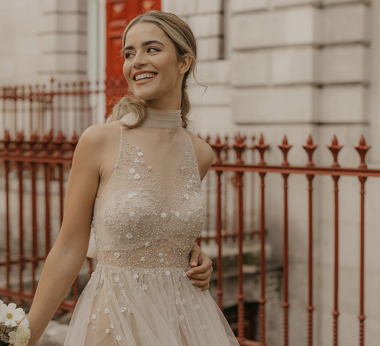 Blonde bride with natural makeup and swept back hair in a tulle halterneck wedding dress with embellished bodice and full skirt 