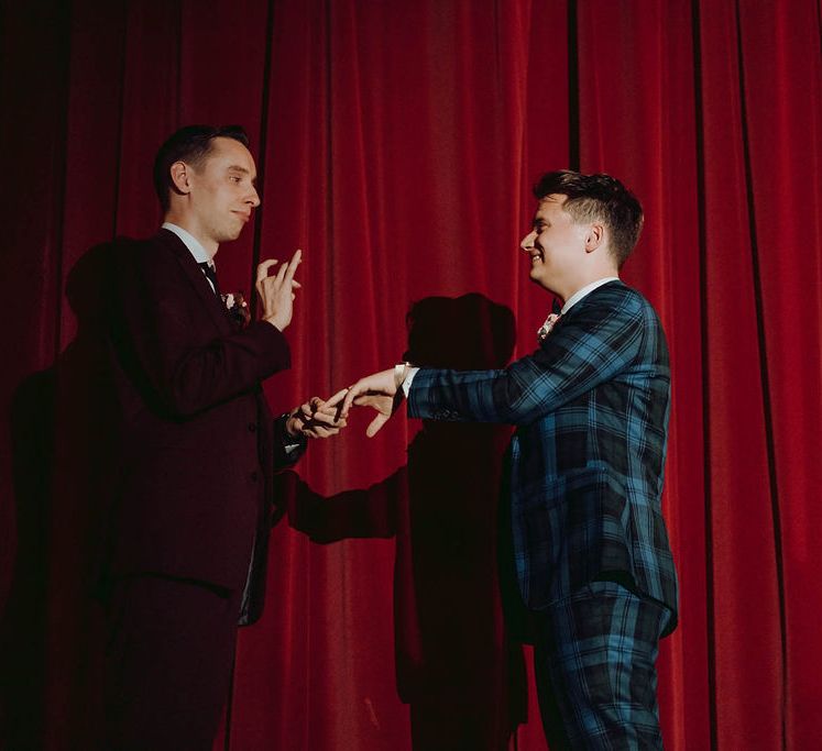 Grooms stand in front of red curtain during cinema wedding | Kim Williams Weddings