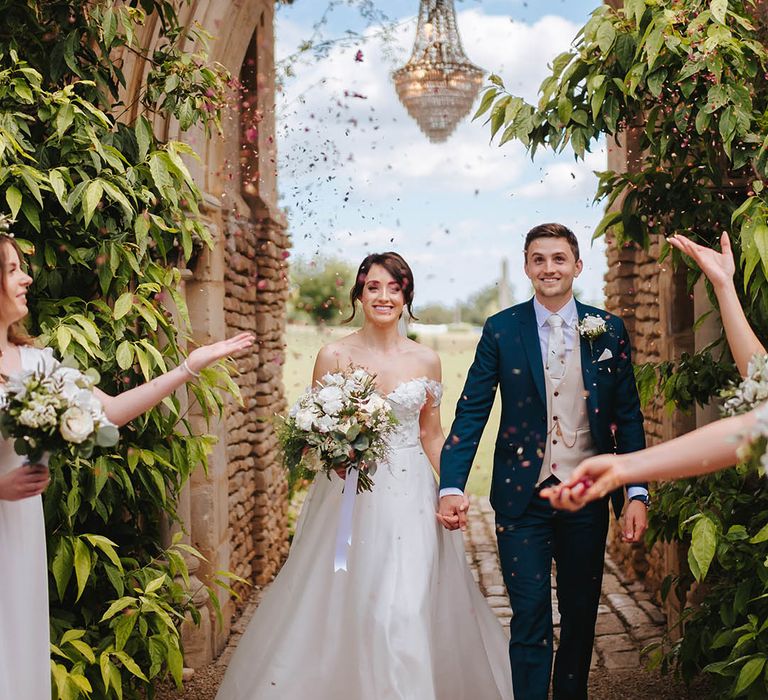 Bride & groom walk through archway at Euridge Manor whilst wedding guests throw confetti around them