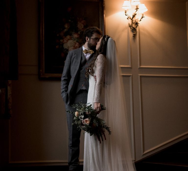 Bride and groom kiss on stairs of stately home