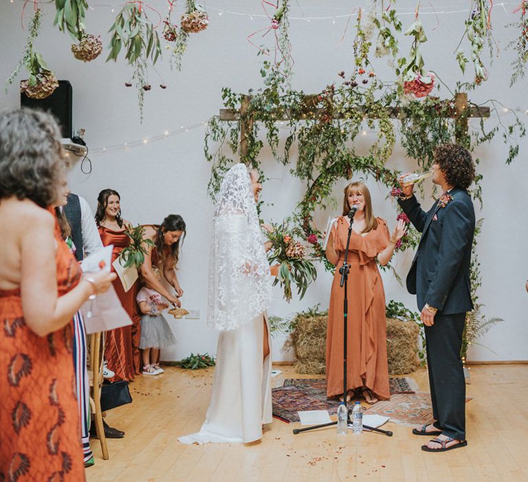 Bride & groom during beach wedding Devon complete with hanging colourful foliage and florals