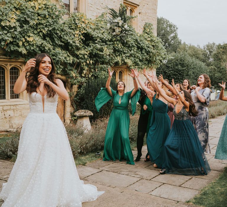 Bride in white Pronovias wedding dress and Jimmy Choo wedding shoes throws white and green bridal bouquet to bridesmaids in green bridesmaid dresses and wedding guests at Notley Abbey wedding