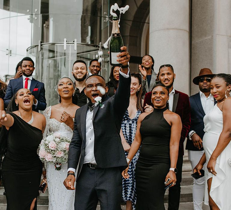 Groom pops champagne on his wedding day in front of wedding party