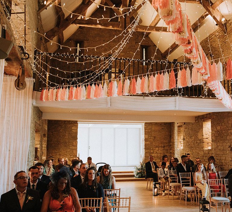 Guests await brides arrival under tassel bunting at barn venue