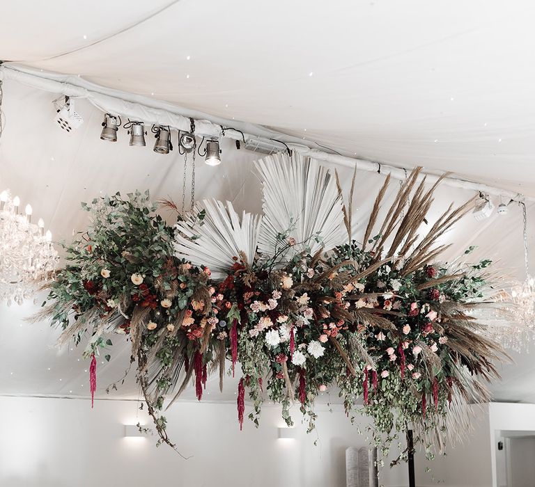 Wedding reception with hanging floral installation including dried and fresh flowers and palm leaves