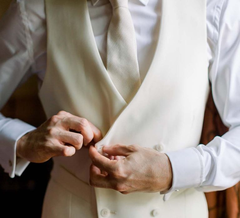 Groom does up his waistcoat on his wedding day