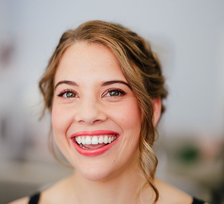 Bride with coral lipstick and orange eye shadow look smiles at the camera