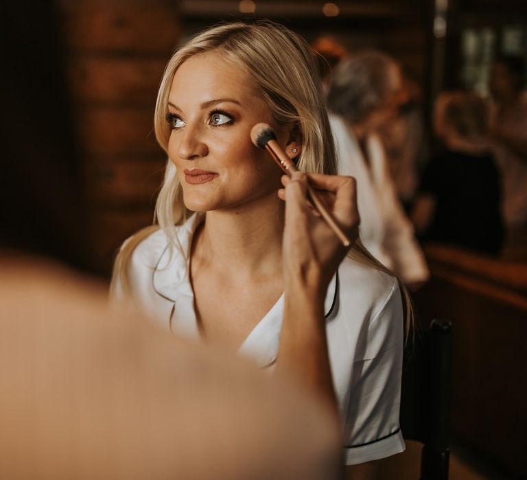 Bride in satin pyjamas has her make up done before barn wedding