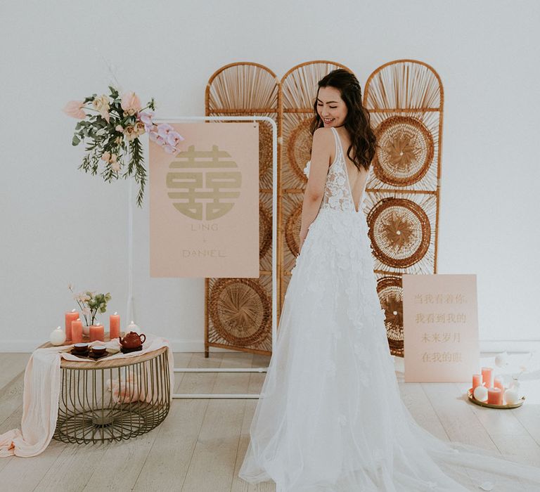 Asian bride in an appliqué wedding dress smiles with bamboo prop and statement asian decor 