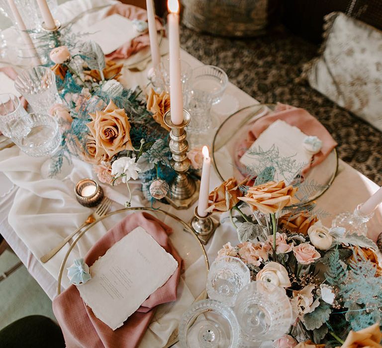 Birdseye view of a wedding reception table styling and decor with pink linens, gold candlesticks, glass charger plates, cut glass goblets and floral arrangements 