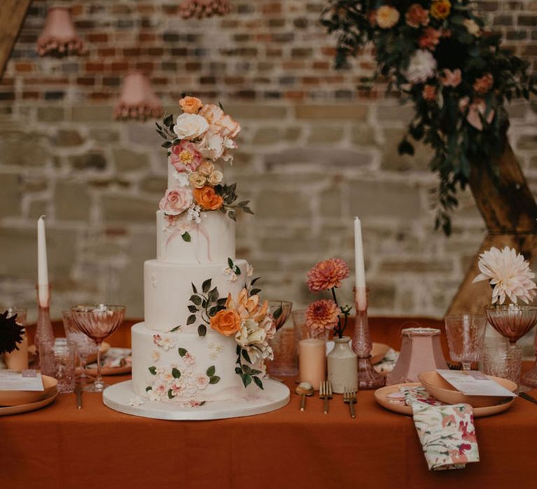 Four tier iced wedding cake with flower decor on a wedding reception table with lampshades, candles and flower decor 