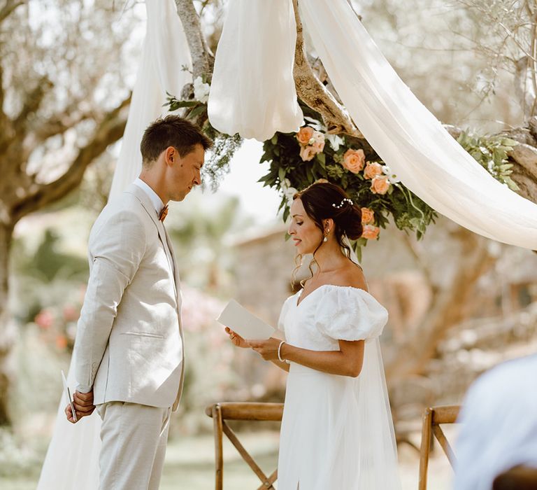 Bride in puff sleeve dress reads wedding vows to husband in beige suit 