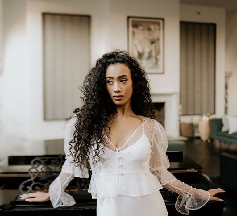 Black bride with long naturally curly hair wearing a satin slip wedding dress and sheer pearl embellished jacket with bell sleeves