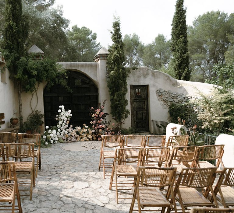 Gorgeous outdoor destination wedding in Barcelona, Spain with wooden rattan chairs for guests and flower display at the altar