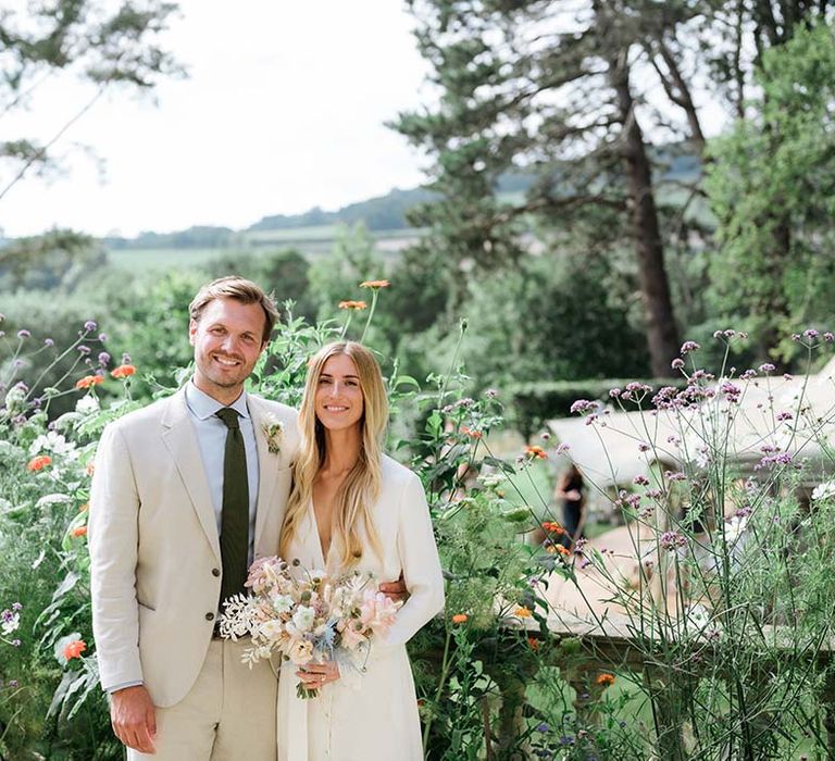 Bride in bespoke Bon Bride wedding dress with groom in cream suit pose together with views of their garden