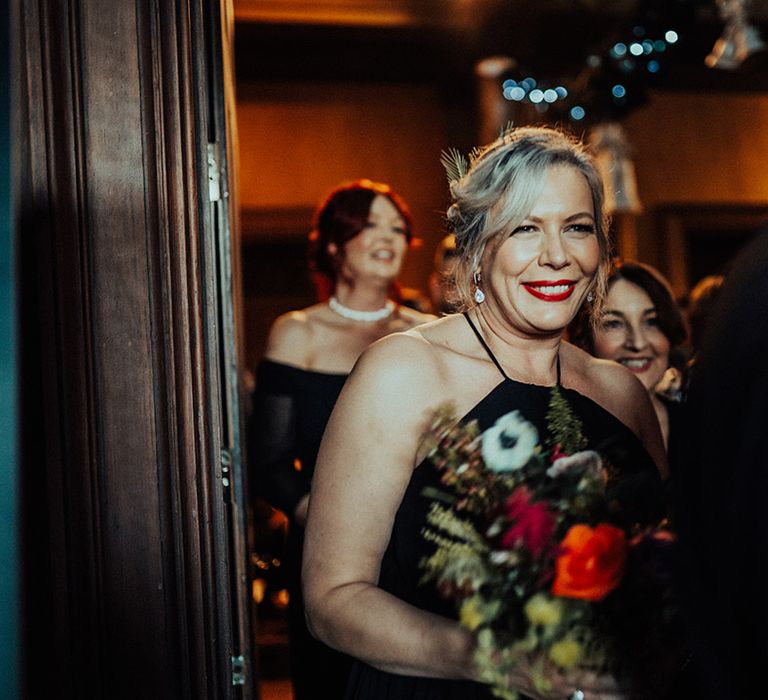 Bridesmaids in dark dresses and bold red lips enter the Castle Leslie Estate venue