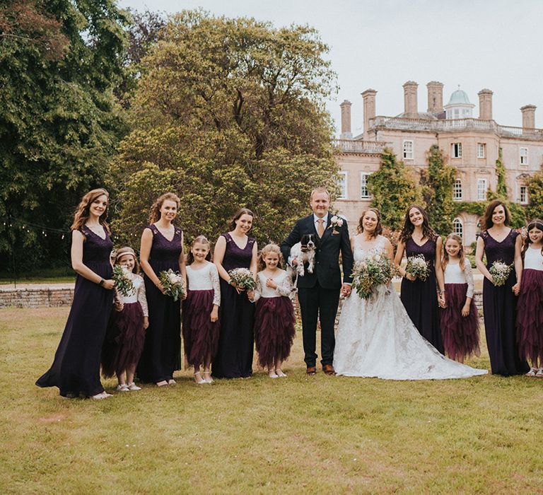 Bride and groom with their dog, six flower girls in purple dresses and six bridesmaids in deep purple dresses