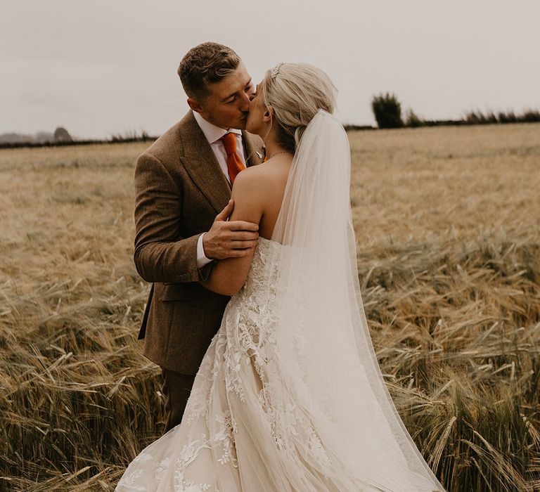 Bride in strapless sweetheart wedding dress with veil kisses groom in autumnal style suit 