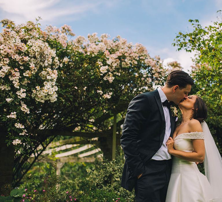 Bride and groom in classic style share a kiss in the gardens of their wedding venue