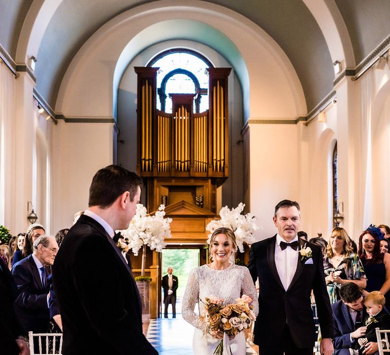 Father of the bride in black tie walks her down the aisle to meet the groom in black tie