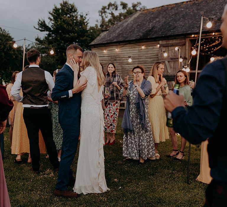 Bride and groom dance outside together with guests dancing all around them for summer rustic barn wedding