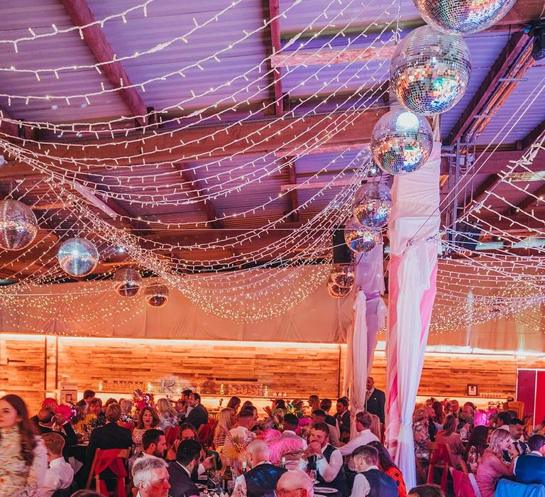 Party festival style wedding reception with fairy lights and disco balls with pink feather and fern leaf centrepiece