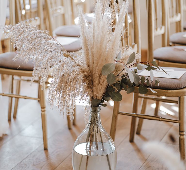 Dried grass and green foliage in glass vases for aisle decoration for boho luxe styled wedding in hotel venue