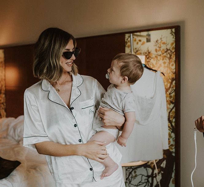 Bridal preparations for the wedding day with bride in satin pyjamas holding baby 