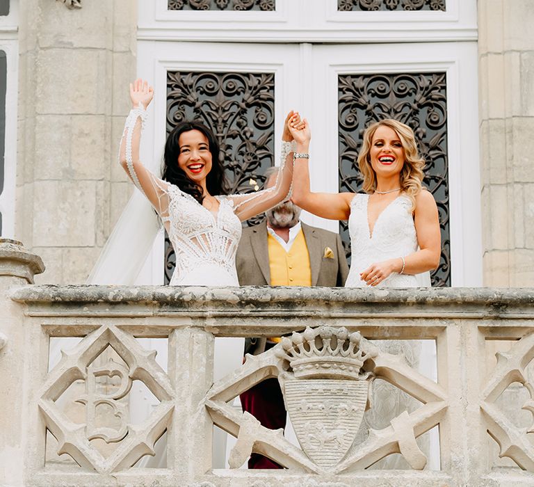 Brides raise their joint hands for guests to see as they are married with both wearing matching red lipstick and lace dresses 