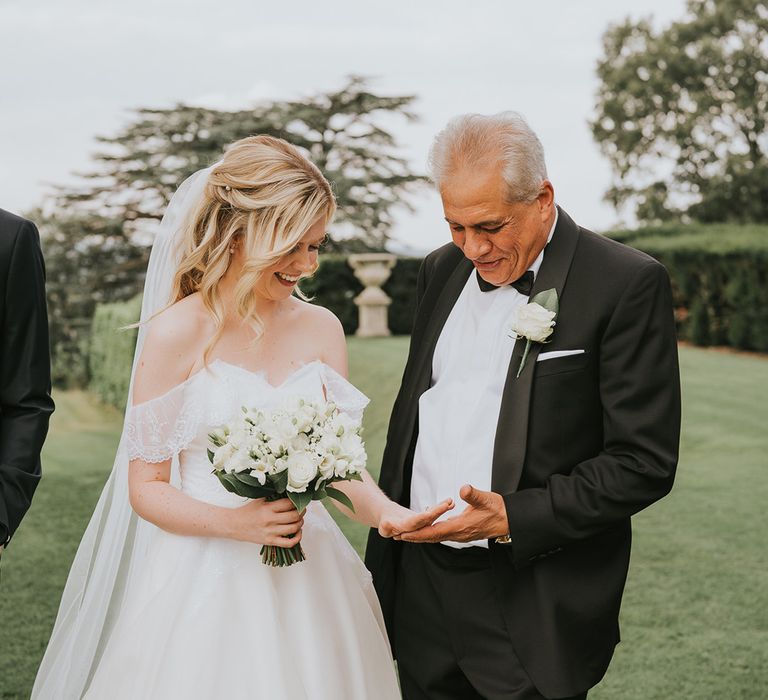 Bride in off the shoulder wedding dress shows off her ring to wedding guest in black tie 