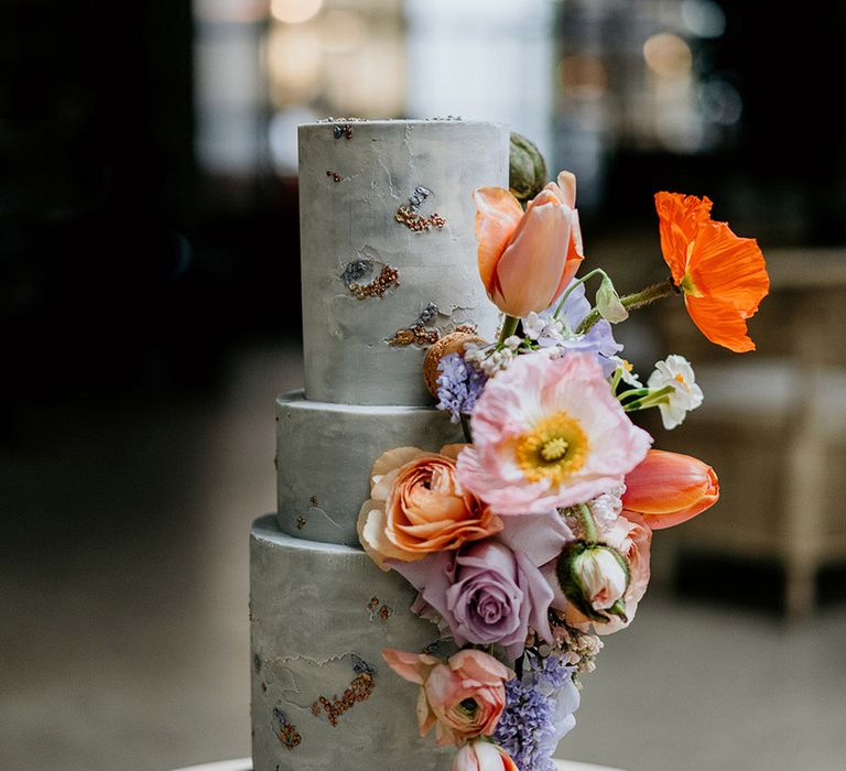 Three tier blue iced cake with colourful pink, purple and orange flowers with shiny detail 