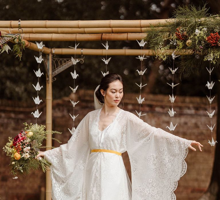 East Asian bride in a lace Kimono-style wedding dress with long sleeves tied with yellow ribbon at Japanese wedding at Gorse Hill