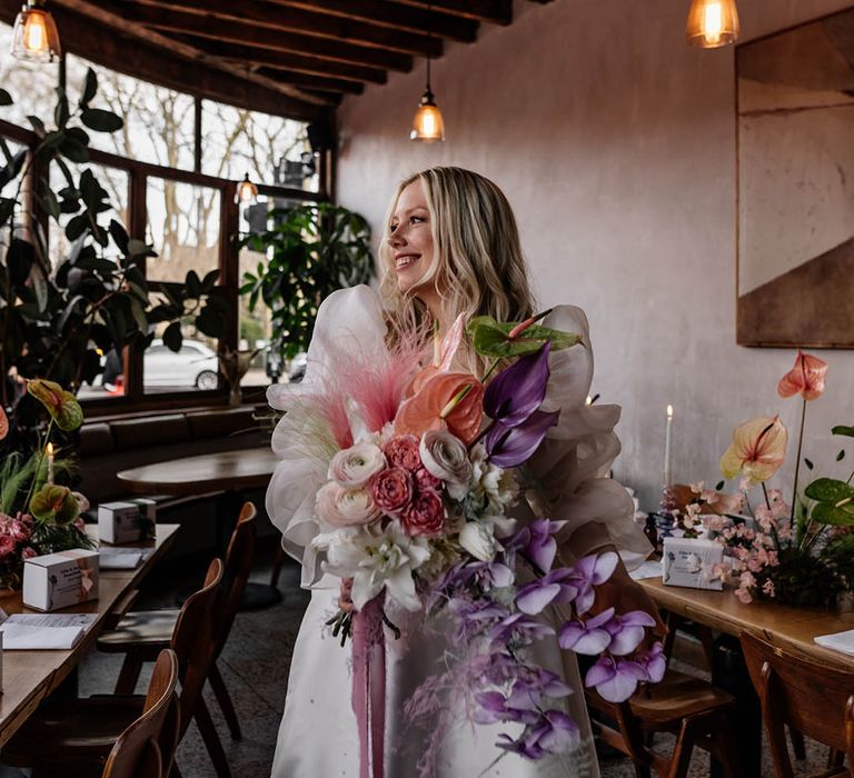 Bride in a JESUS PEIRO wedding dress with voluminous sleeves holding a pastel pink, lilac and white wedding bouquet with orchids, anthuriums and ranunculus flowers