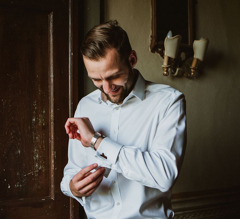 Groom does up his cufflinks on the morning of his wedding day in Tuscany 