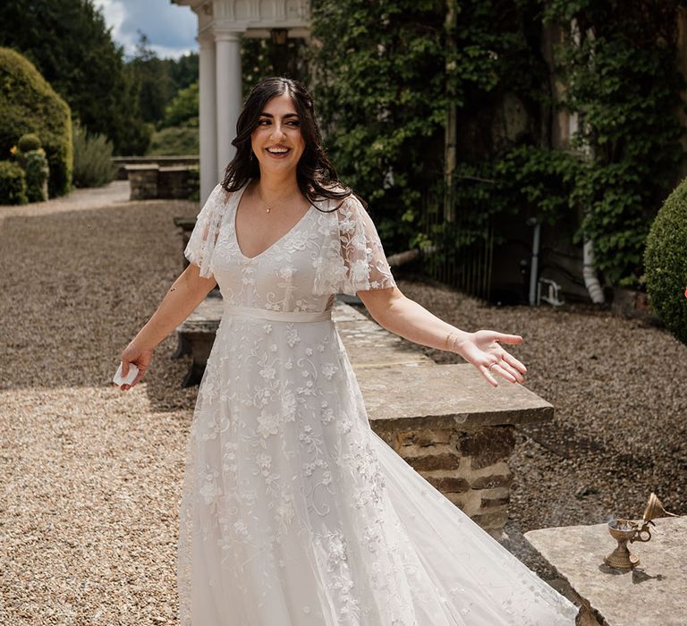 Bride wearing Anna Campbell wedding dress with short sheer sleeves finished with floral embellishment and silk waistband 