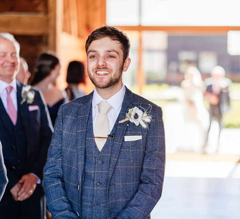 Groom in blue checkered suit with pale tie and gold tie clip smile as he waits for the bride 