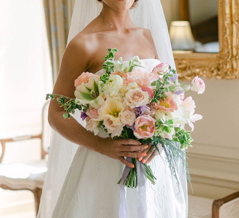 Bride wearing a beaded headband in a strapless wedding dress with coral pink wedding nails holding a pastel bouquet 