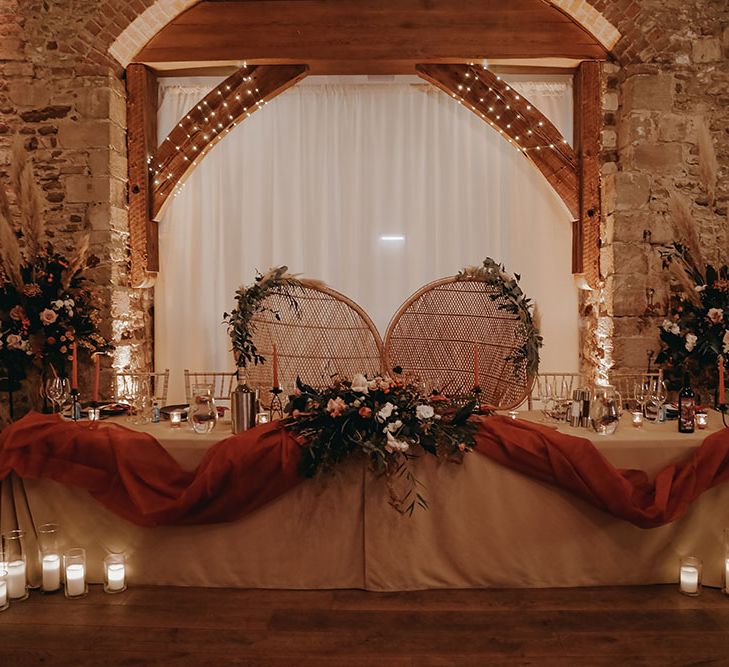 Sweetheart table with wicker chairs and Autumnal colour scheme with orange fabric to the front of table and large dried floral arrangements 