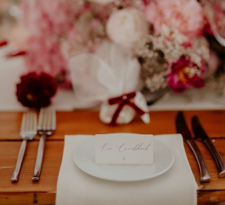 White and pink wedding flowers with white fabric napkins and white name place cards with black calligraphy writing