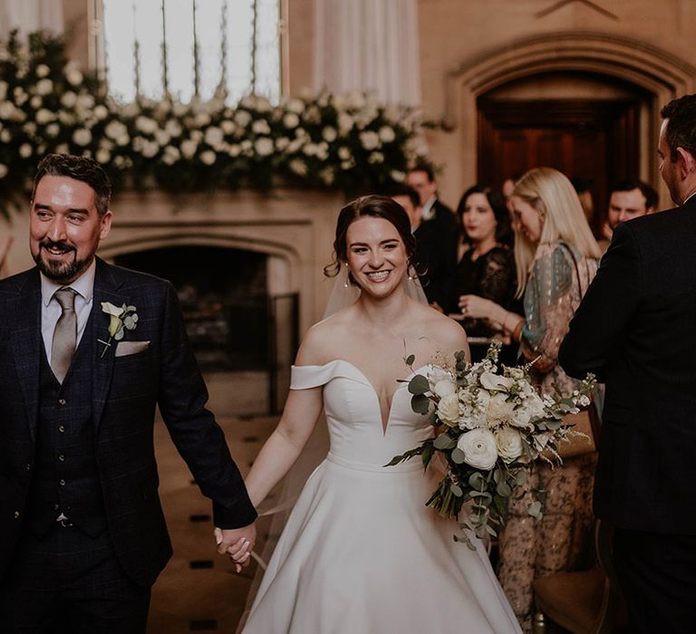 Groom in dark blue suit walks back down the aisle with the bride as a married couple