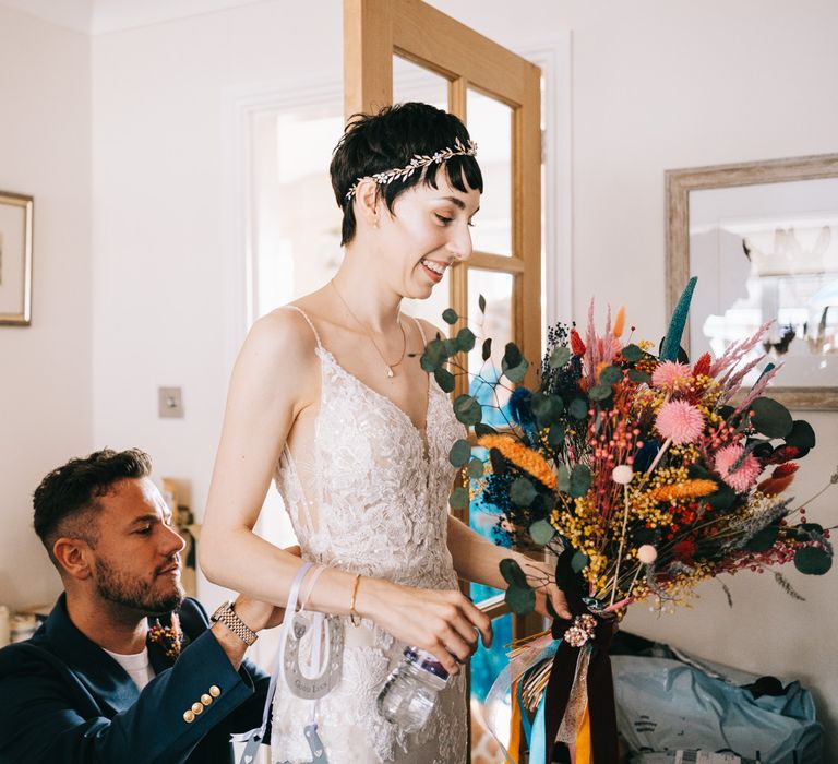 Bride holds dried colourful floral bouquet and wears lace Enzoani wedding dress